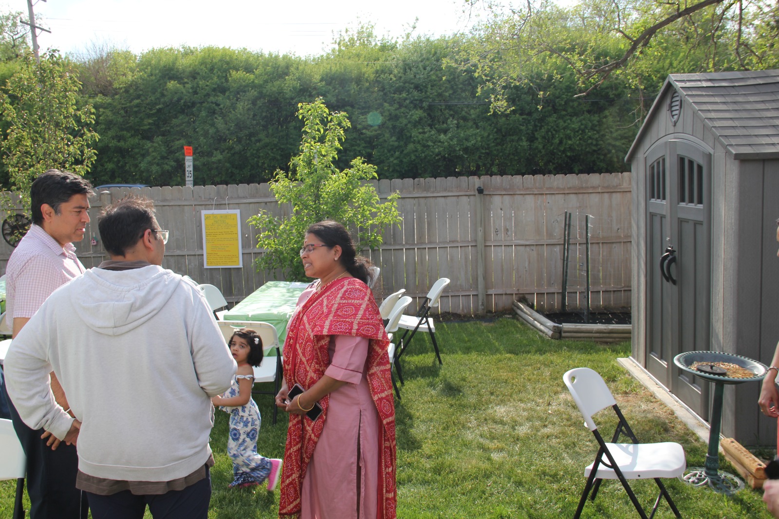 Guests in conversation near the FMSC project info poster with shed and raised beds behind