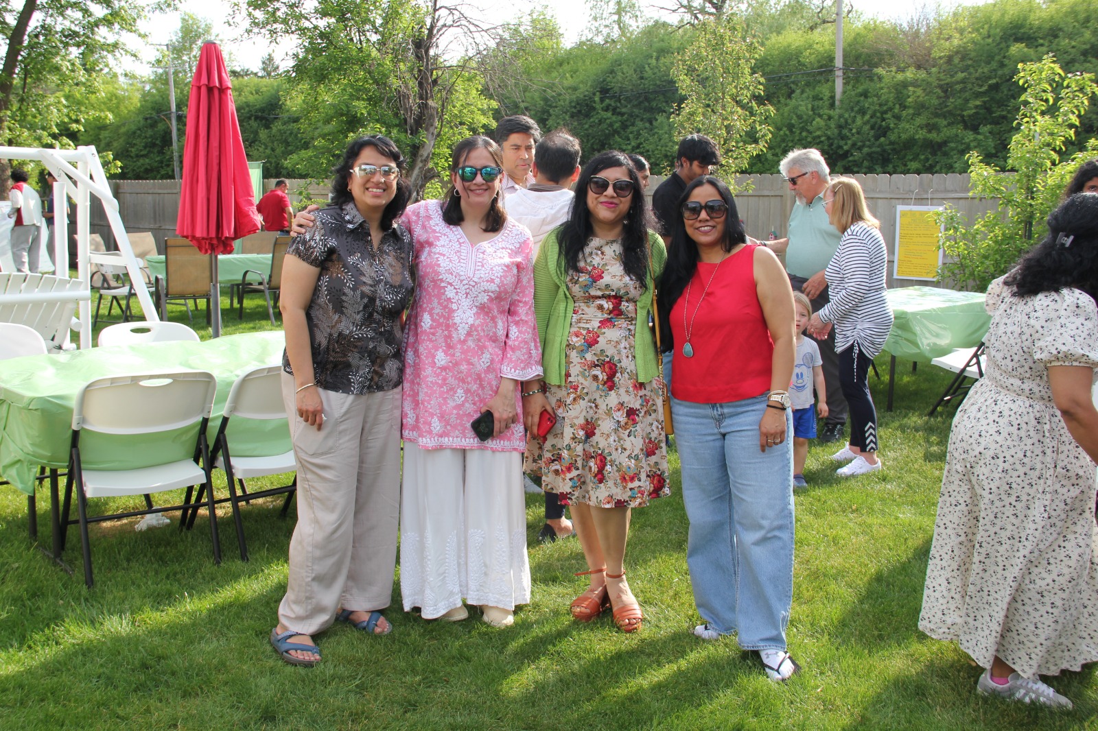 Four women friends posed together in front of the event setup with green tables behind