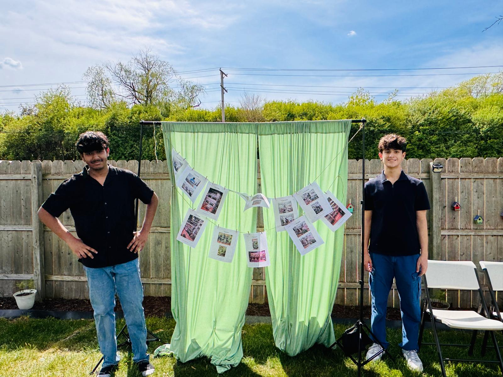 Two student leaders posed beside the green photo-rope display showing the project process
