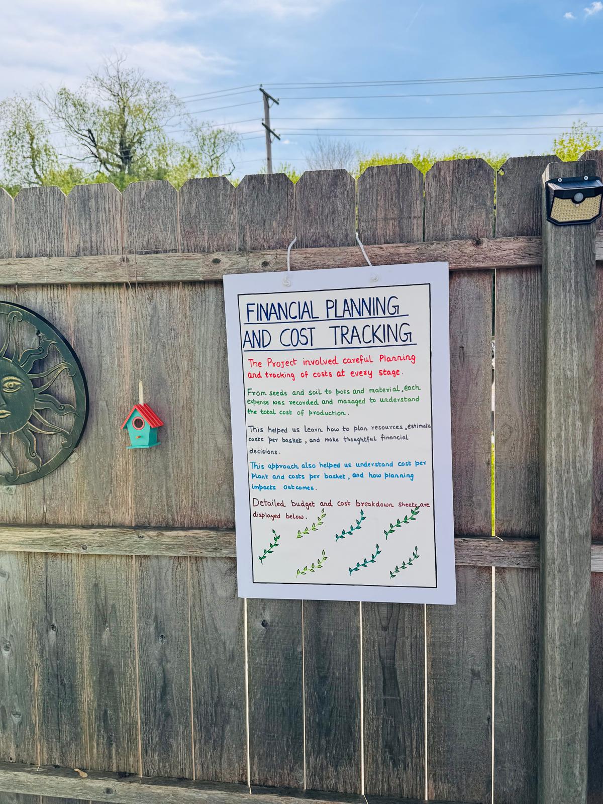 Financial Planning and Cost Tracking board mounted on the fence next to sun medallion and birdhouse