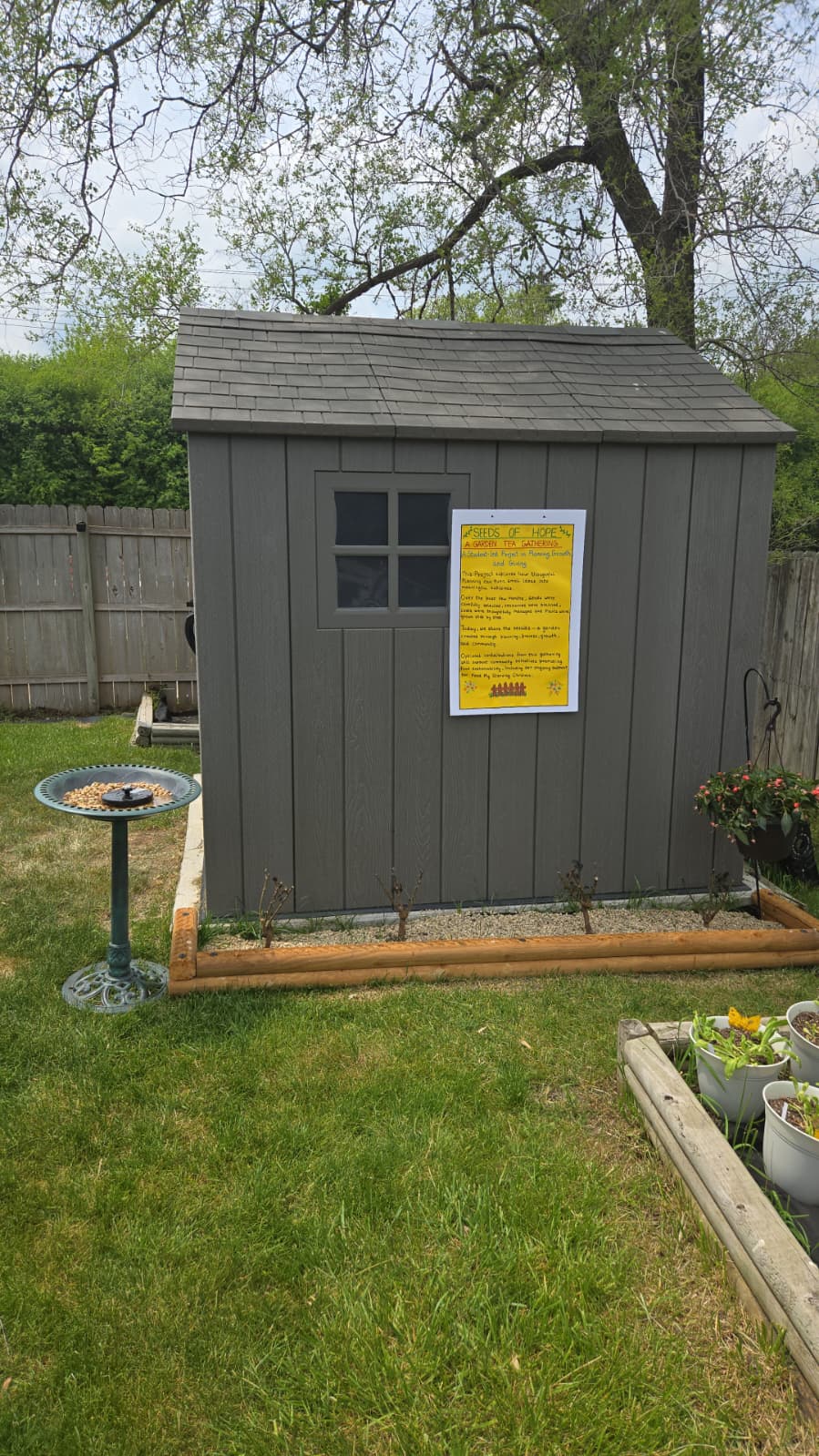 Seeds of Hope welcome board mounted on garden shed with bird feeder and raised beds