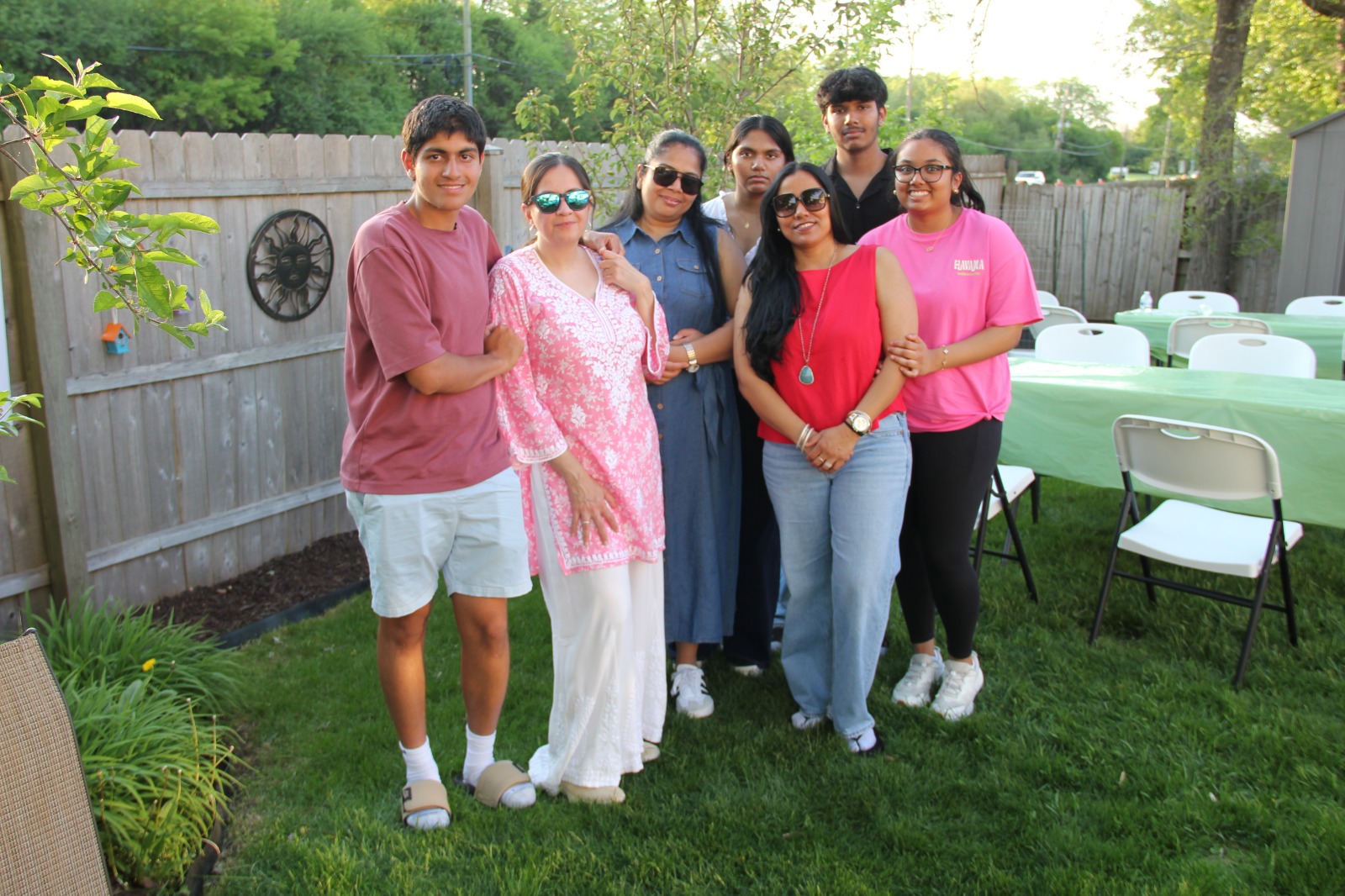Group of teen and adult friends posed together in front of green-clothed event tables