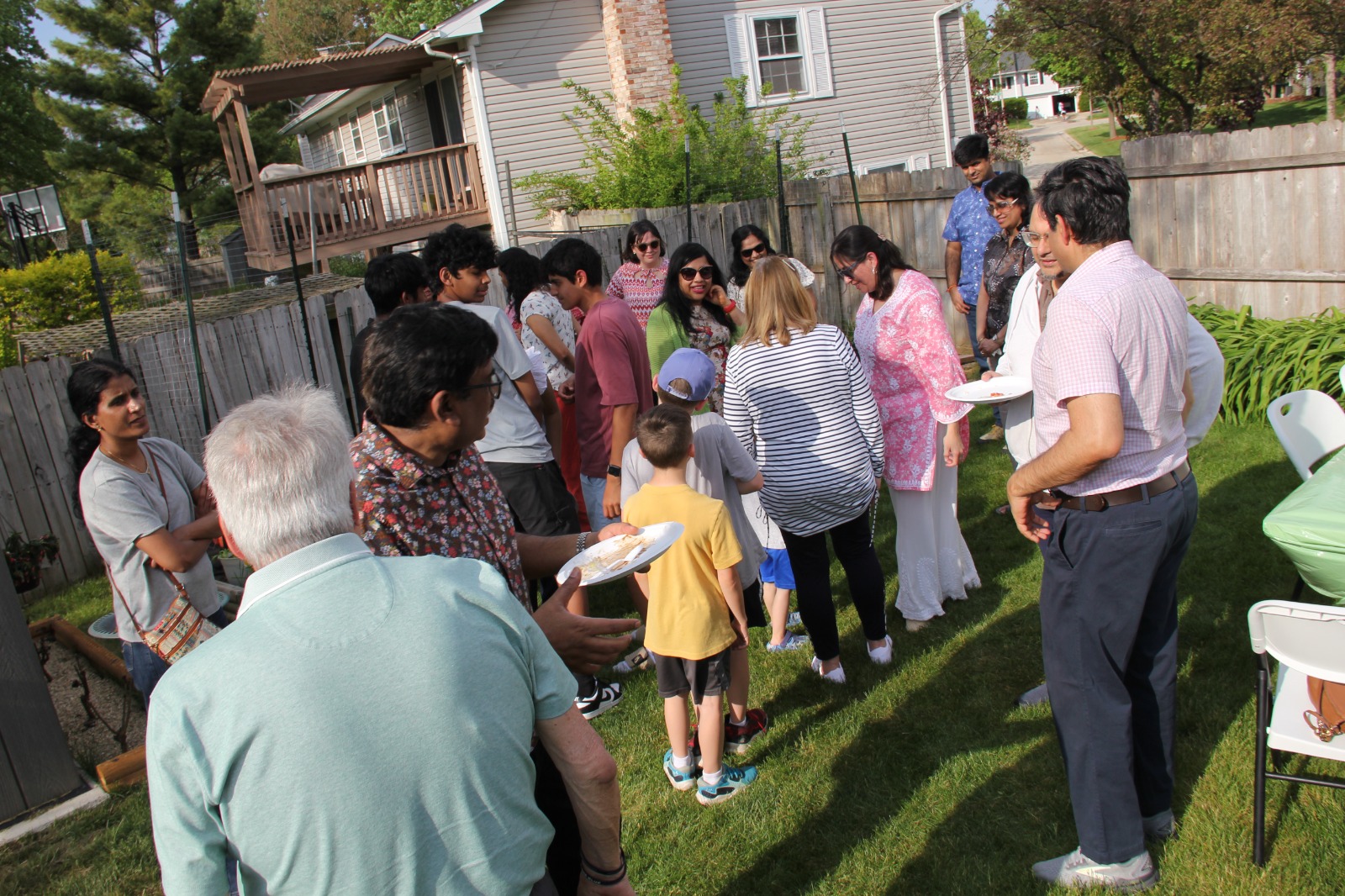 Guests of all ages gathered in the backyard with plates of food waiting for the project presentation to begin