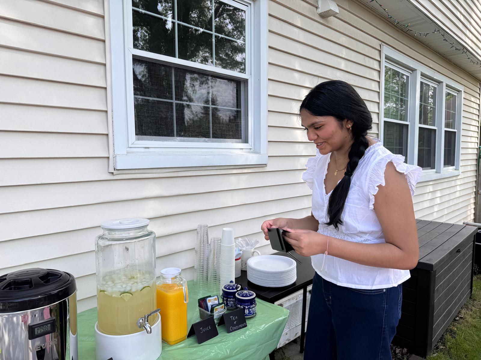 Volunteer hosting the drinks table with lemonade dispenser, juice, tea and condiments