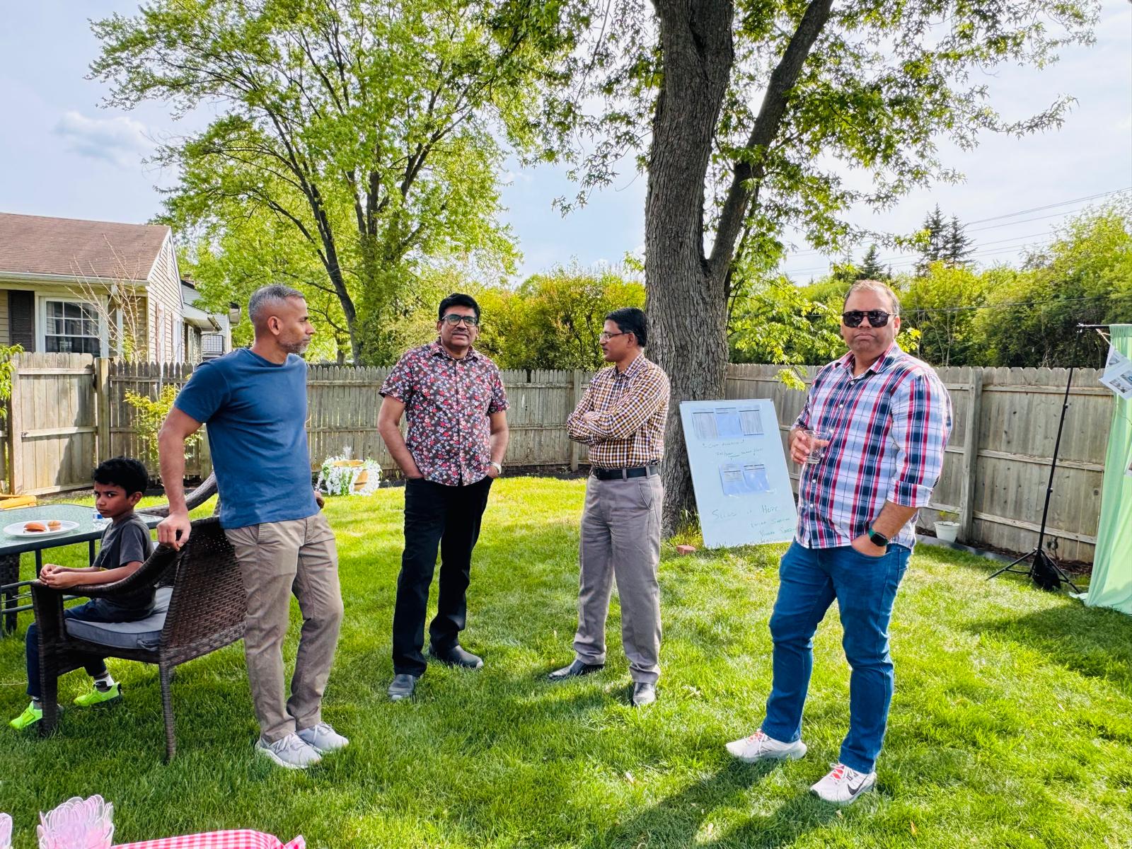 Guests gathered around the project board under the backyard tree discussing the Seeds of Hope project