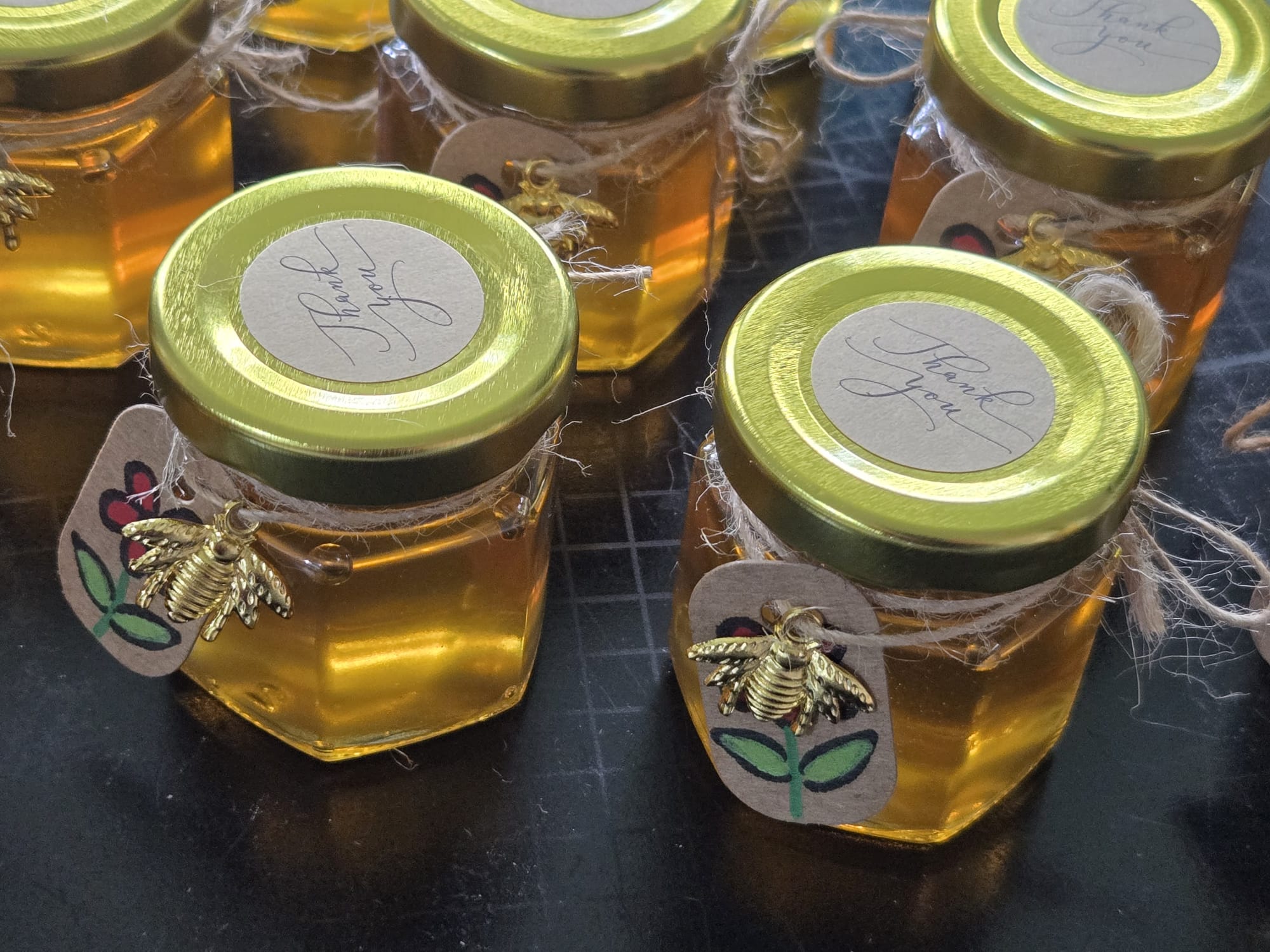 Mini Thank You honey jars with gold bee charms and hand-painted flower tags as guest gifts