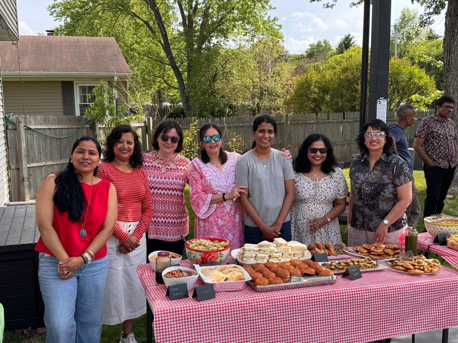 Seven women friends posed behind the buffet table with sliders, sandwiches, baba ganoush and chaat