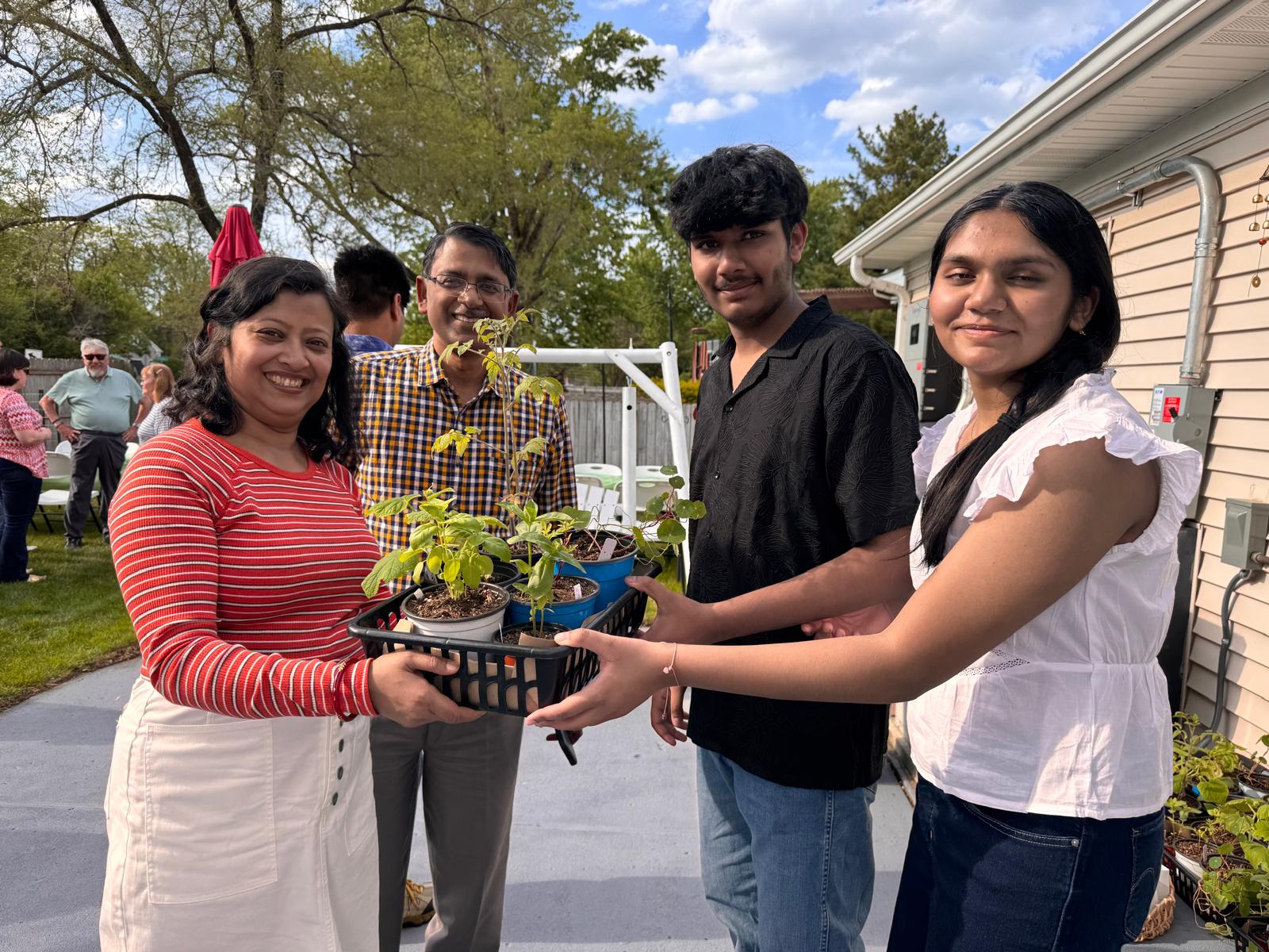 Host family with mom, dad and two teens handing off a plant giveaway basket in the driveway