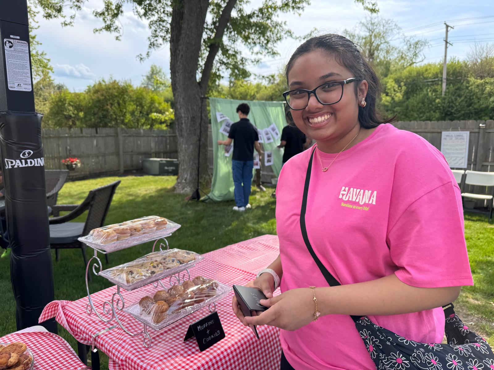 Student host smiling at the dessert table with tiered tray of muffins and cookies