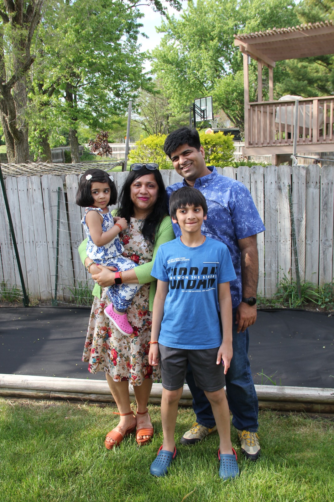 Family of four posed together in the backyard with trampoline and pergola in background