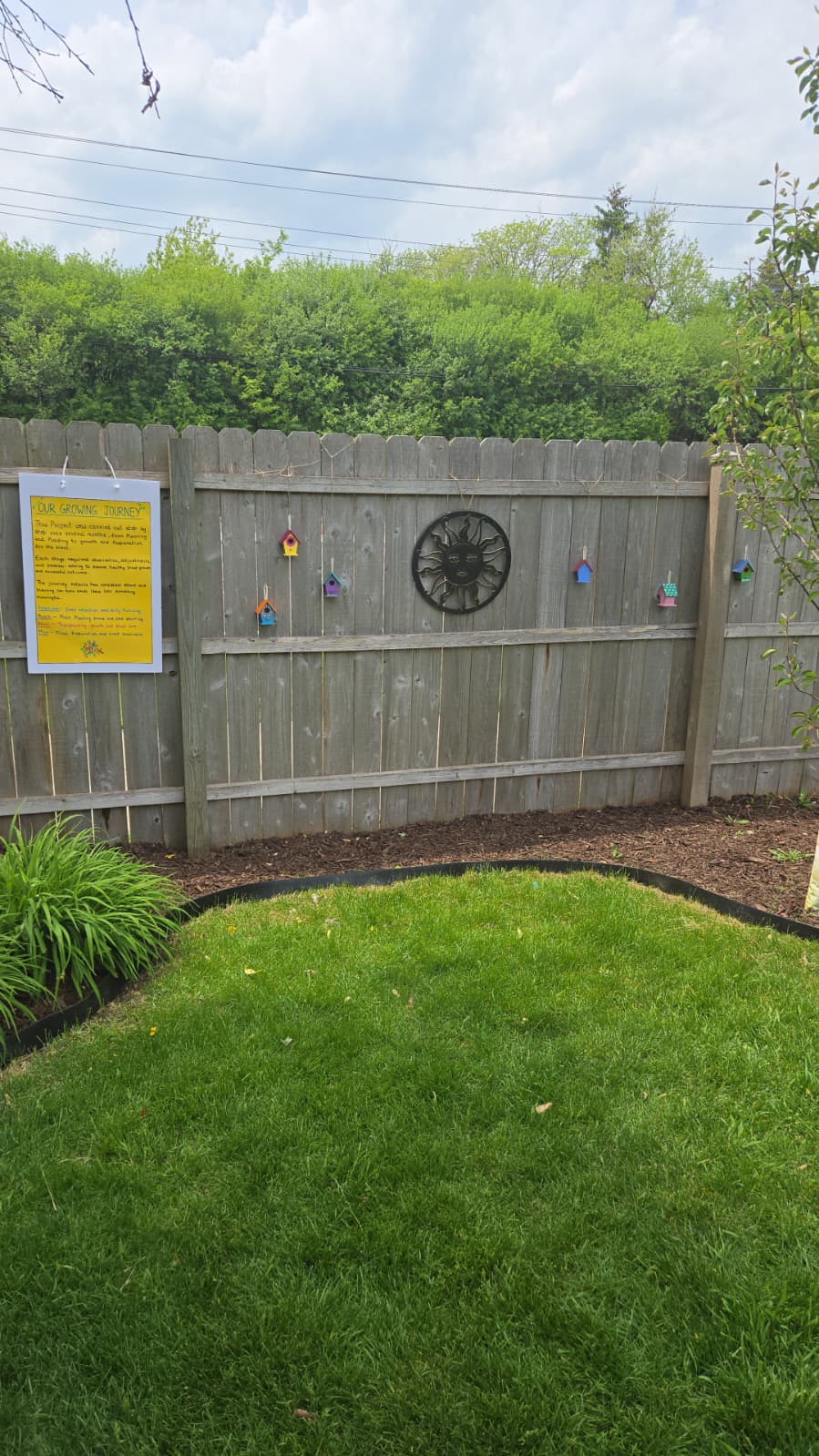 Our Growing Journey board on fence with painted birdhouses and sun medallion display