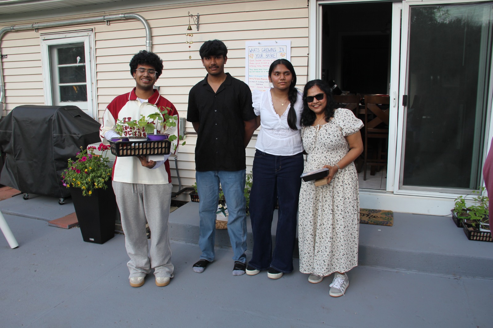 Four guests posed on the patio holding a strawberry and herb giveaway basket beside the menu board